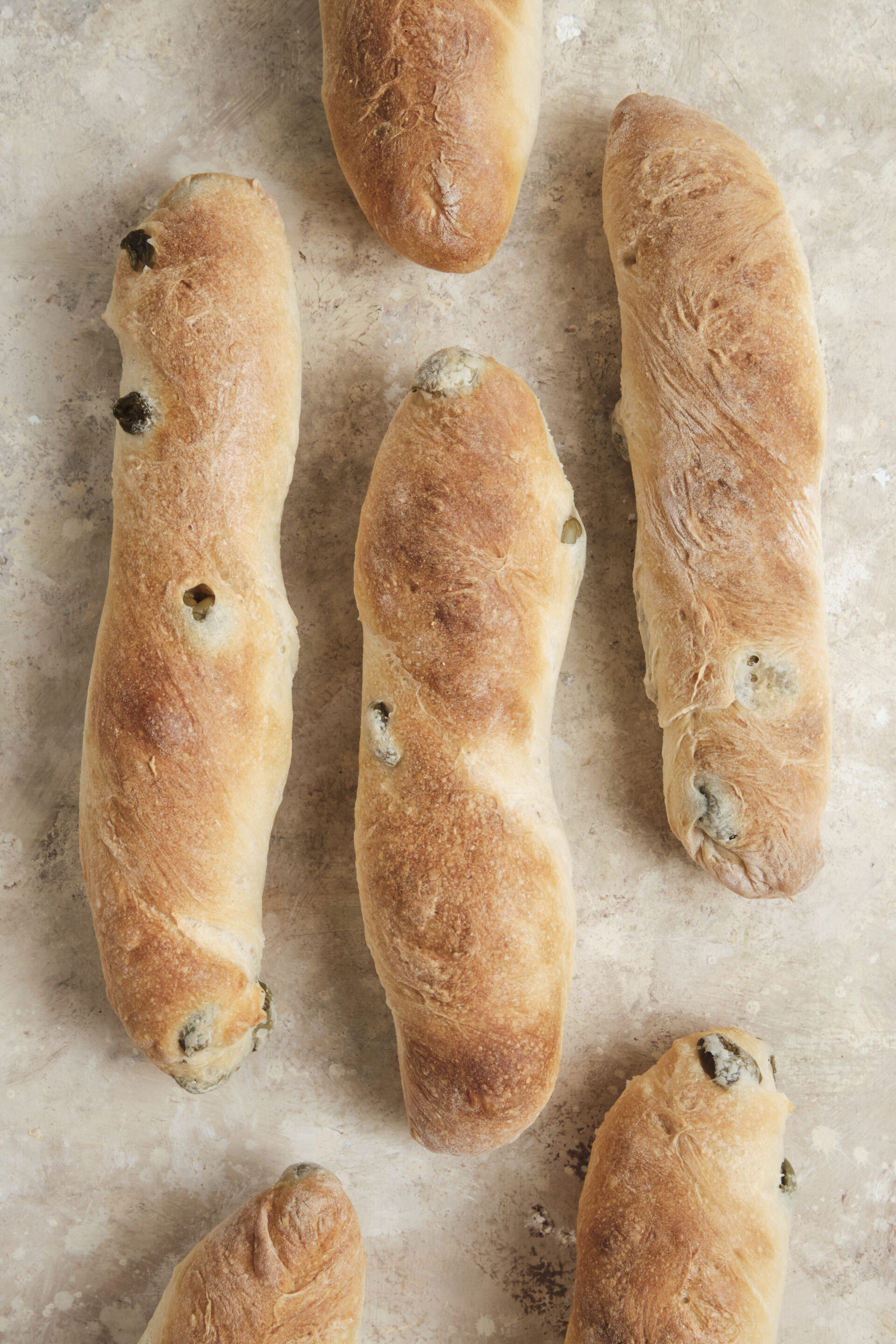 A close-up shot of an olive baguettes packed with chopped green olives and a perfectly golden, crispy crust.