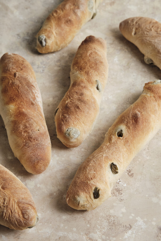 Freshly baked olive baguettes with a golden, crispy crust and tender crumb, studded with olives and served on a rustic wooden table.