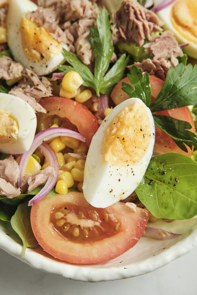 Close-up of a vibrant tuna salad showing texture, featuring hard-boiled egg quarters, juicy tomatoes, and corn kernels.
