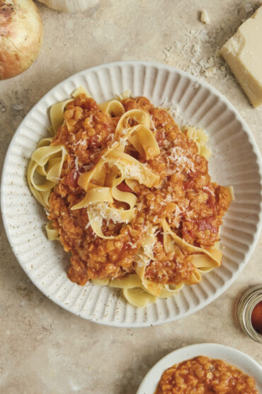 Hearty vegan lentil bolognese sauce served over a bed of wide tagliatelle pasta in a deep plate, set against a rustic background.
