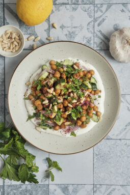 A refreshing roasted chickpea and cucumber salad with fresh herbs and a creamy tahini dressing, beautifully served on a plate and topped with toasted pine nuts.