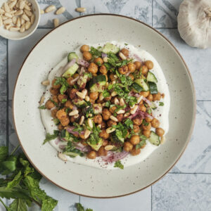 A refreshing roasted chickpea and cucumber salad with fresh herbs and a creamy tahini dressing, beautifully served on a plate and topped with toasted pine nuts.