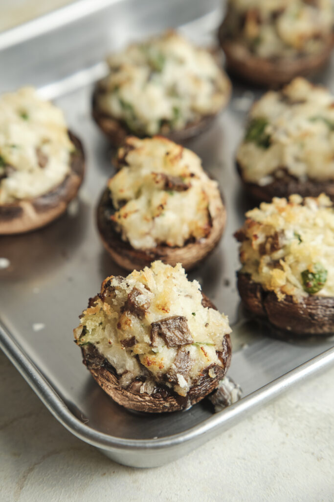 Golden baked stuffed mushrooms filled with a creamy cheese and herb mixture, topped with Parmesan and crispy breadcrumbs, served on a platter.