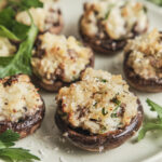 Golden baked stuffed mushrooms filled with a creamy cheese and herb mixture, topped with Parmesan and crispy breadcrumbs, served on a platter.
