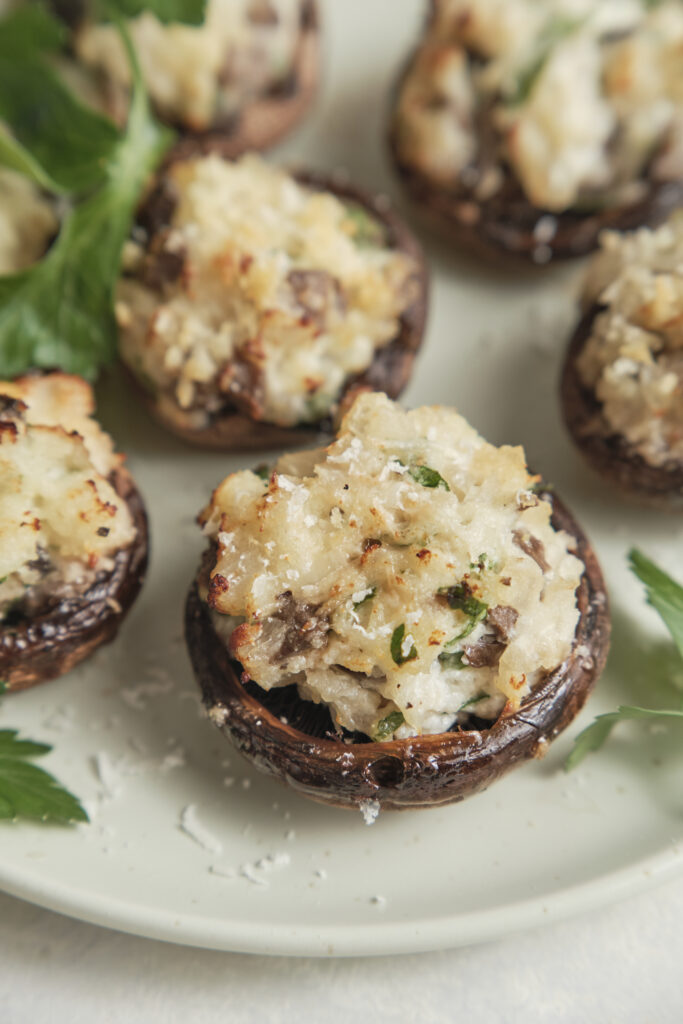 Golden baked stuffed mushrooms filled with a creamy cheese and herb mixture, topped with Parmesan and crispy breadcrumbs, served on a platter.