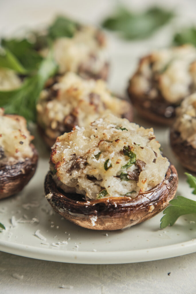 Golden baked stuffed mushrooms filled with a creamy cheese and herb mixture, topped with Parmesan and crispy breadcrumbs, served on a platter.