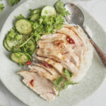 Sliced poached chicken served over fragrant jasmine rice with side dipping sauces and cucumber slices.