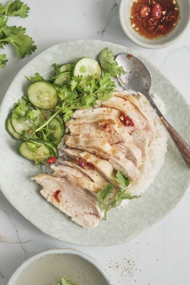 Sliced poached chicken served over fragrant jasmine rice with side dipping sauces and cucumber slices.
