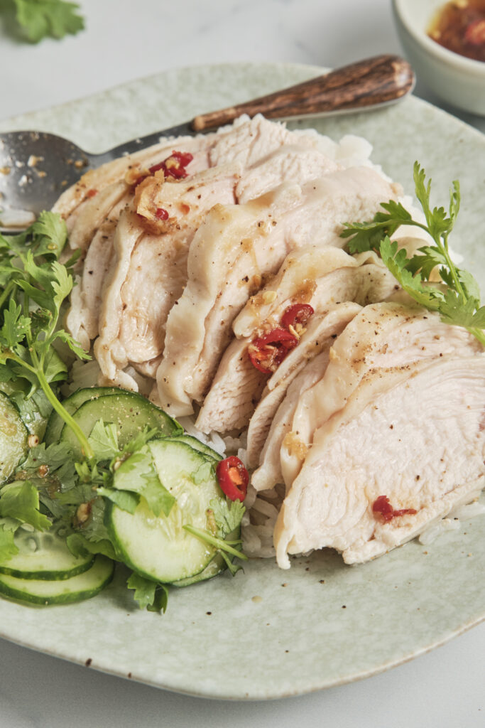 Tender slices of poached chicken over savory jasmine rice, accompanied by traditional dipping sauces and crisp cucumber.