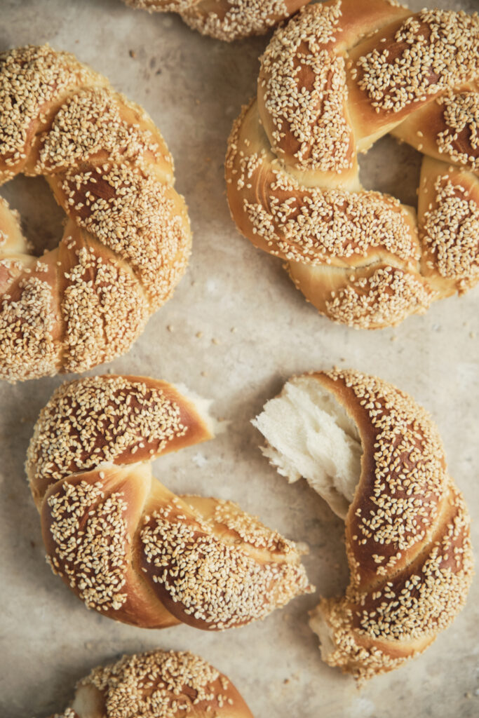 A sesame-crusted Turkish simit broken apart on a rustic background, showing the soft inside texture of the bread.