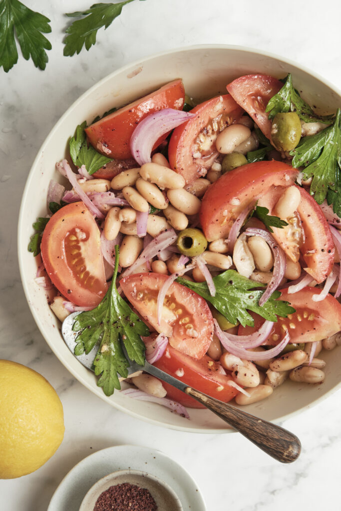 Close-up shot of a Mediterranean white bean salad with vibrant red tomatoes, green olives, and fresh minced herbs.