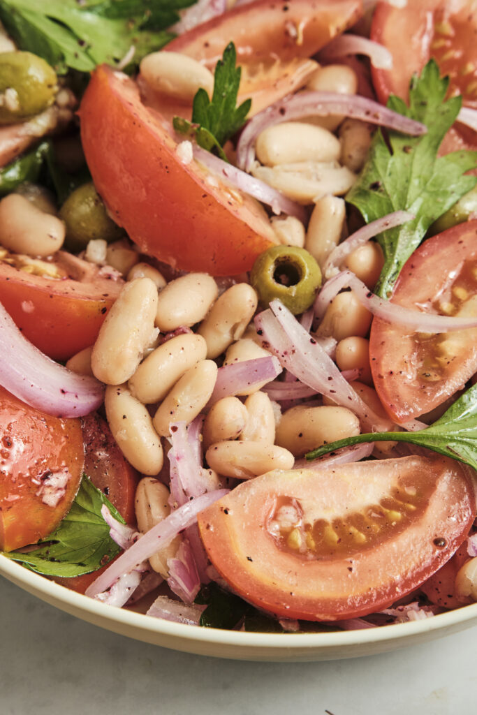 Close-up shot of a Mediterranean white bean salad with vibrant red tomatoes, green olives, and fresh minced herbs.