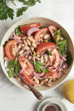 A traditional Turkish white bean salad (Piyaz) served in a shallow bowl, featuring creamy cannellini beans tossed with juicy diced tomatoes, fresh chopped parsley, and briny green olives, all lightly coated in a zesty dressing.