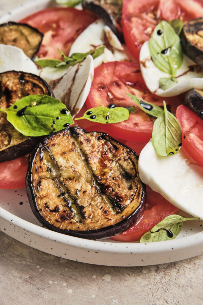 Close-up of an Italian eggplant Caprese with layers of roasted eggplant, fresh mozzarella, juicy tomatoes, and basil, finished with a glossy drizzle of balsamic glaze, highlighting the vibrant colors and fresh textures.