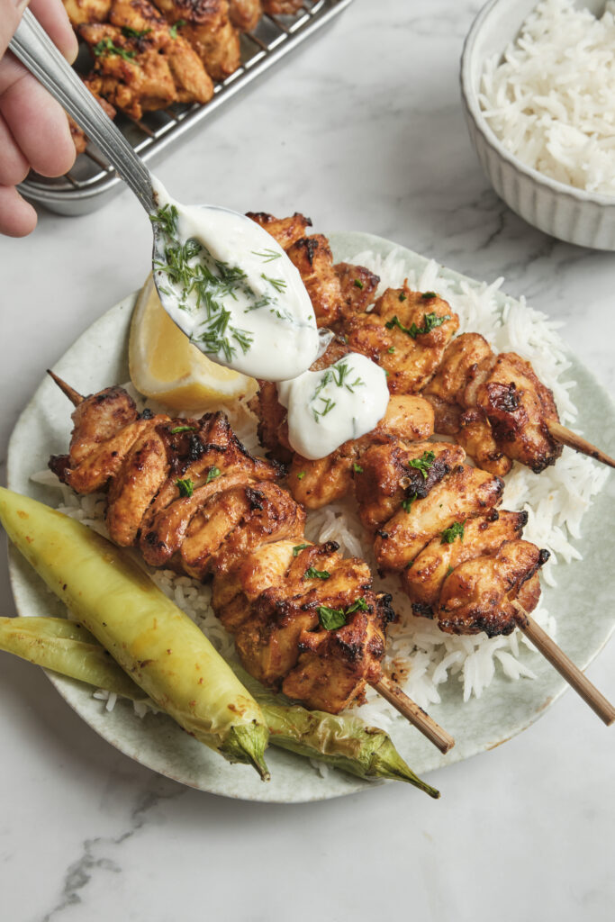 Grilled shish tawook skewers with juicy marinated chicken pieces, charred edges, and fresh herbs, served on a plate.
