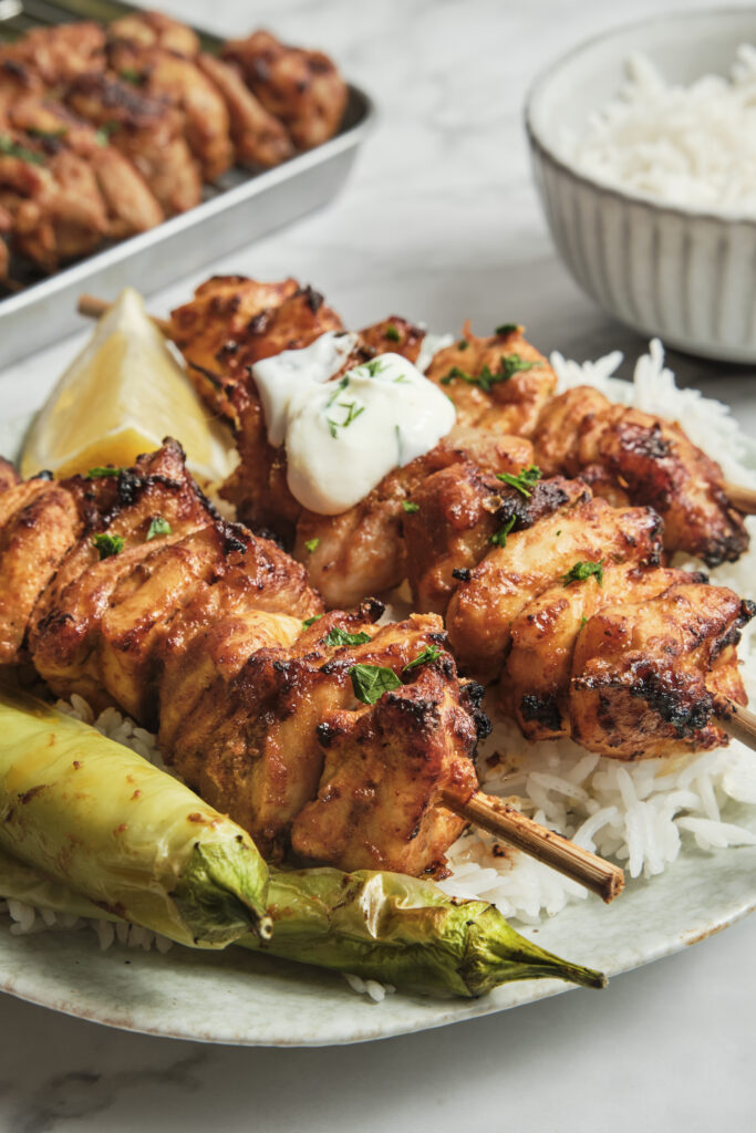 Close up of grilled shish tawook skewers with juicy marinated chicken pieces, charred edges, and fresh herbs, served on a plate.